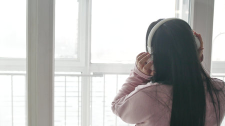 Young woman with headphones listens to music by the windowの写真素材