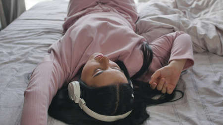 Attractive woman listening to music using headphones on bed at home.の写真素材