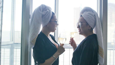 Two young women in sun glasses and towels on their heads drinking sompagne in a hotel room.