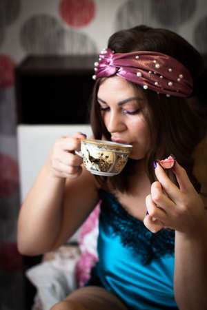 A beautiful woman in home clothes enjoying sweets and tea at homeの写真素材
