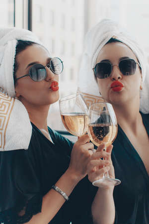 Girlfriends are celebrating the brides bachelorette party. Two women in robes, sunglasses and towels on their heads are holding glasses of champagne.の写真素材