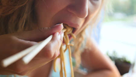 Woman eating delicious udon in an Asian cuisine restaurant. Woman eating noodles with vegetables and seafood with sushi chopsticks. Delicious dinnerの写真素材