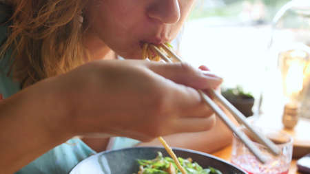Woman eating delicious udon in an Asian cuisine restaurant. Woman eating noodles with vegetables and...