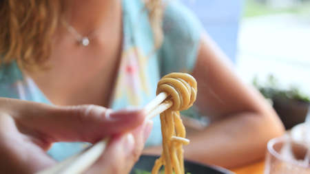 Woman eating delicious udon in an Asian cuisine restaurant. Woman eating noodles with vegetables and...