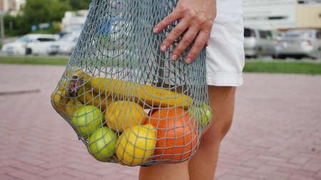 Close-up of a woman walking with a reusable eco-bag full of fruits. A woman carries groceries in a...