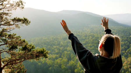 A woman traveler stands on the top of a mountain near the banks of the Mana River in Siberia and...
