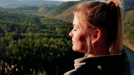 A woman traveler stands on the top of a mountain and stretches out her hands to the sun enjoying a beautiful dayの写真素材