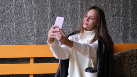 A beautiful woman sits in a cafe and takes a selfie. Casual lifestyle portrait. Businesswoman