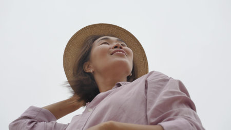 Portrait of a woman traveler against the blue sky. Beautiful Asian woman holds the hat with her...