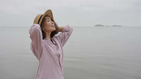 Portrait of a woman traveler against the blue sky. Beautiful Asian woman holds the hat with her hands and enjoys the rest. The concept of feeling happiness, friendly positive.の写真素材
