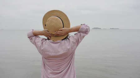 Portrait of a woman traveler against the blue sky. Beautiful Asian woman holds the hat with her hands and enjoys the rest. The concept of feeling happiness, friendly positive.の写真素材