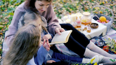 young mother and little daughters on a picnic outdoors reading a book togetherの写真素材