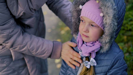 Mom and little girl in warm clothes are walking in the autumn park.の写真素材