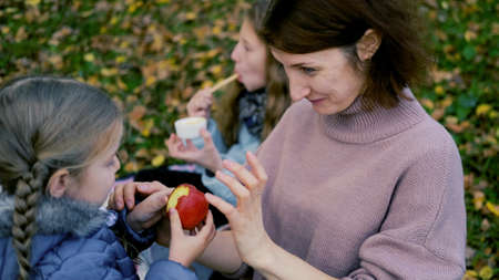 young mother and daughter eat red juicy apples on a picnic in natureの写真素材