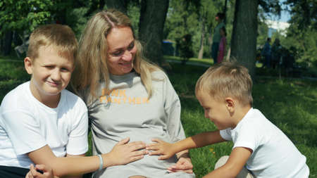 Close up portraits of mom with two sons who are resting in the park on a sunny day