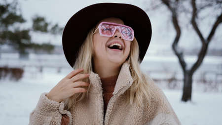 Woman in a beautiful corduroy hat and pink glasses waves her hands at the camera and gives air...