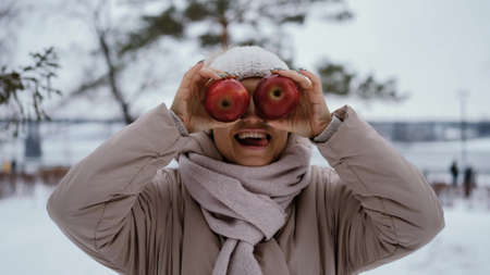 crazy joyful woman makes faces with two apples in her hands against the background of a snowy winter parkの写真素材
