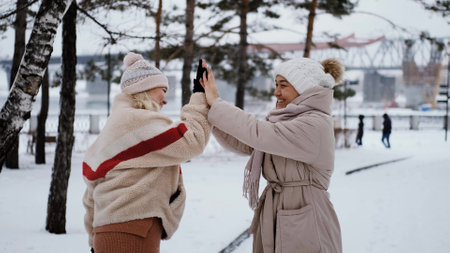 Two lovely women laugh and hug against the background of a snowy winter park. female friendship conceptの写真素材