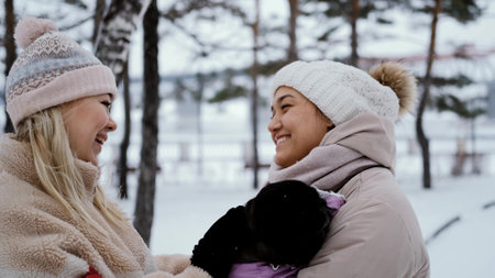 Two lovely women laugh and hug against the background of a snowy winter park. female friendship conceptの写真素材
