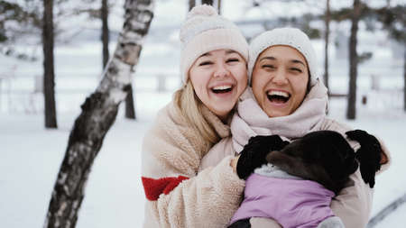 Two lovely women laugh and hug against the background of a snowy winter park. female friendship conceptの写真素材