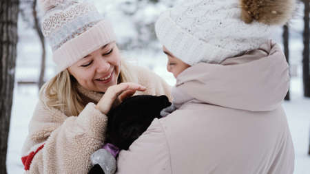 Two lovely women laugh and hug against the background of a snowy winter park. female friendship conceptの写真素材