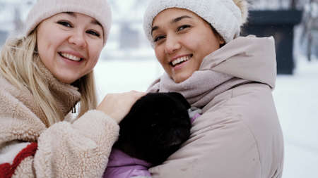 Two lovely women laugh and hug against the background of a snowy winter park. female friendship conceptの写真素材