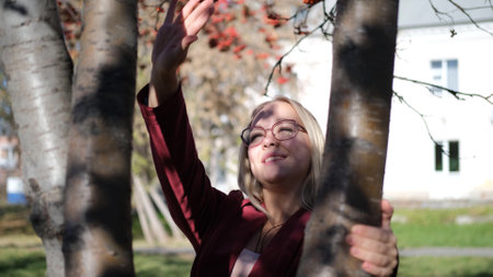 Cute blonde hugs a tree in the autumn city park. Beautiful woman gently hugs a tree trunk in the fall season.の写真素材