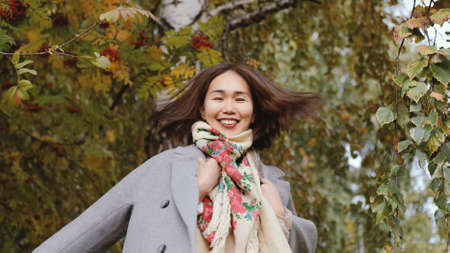 Happy asian woman in gray coat whirls in autumn parkの写真素材