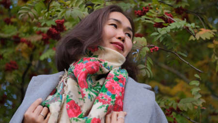 Happy asian woman in gray coat whirls in autumn parkの写真素材