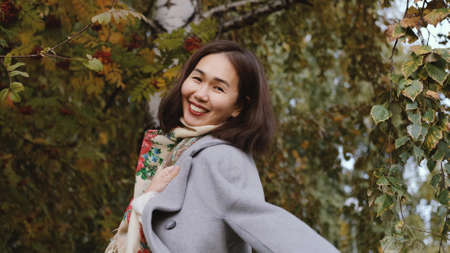 Happy asian woman in gray coat whirls in autumn parkの写真素材