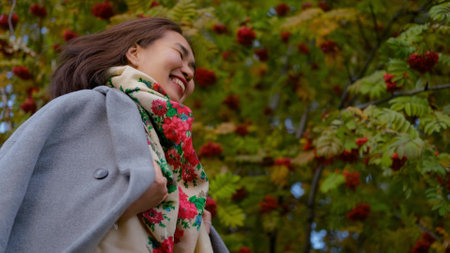 Happy asian woman in gray coat whirls in autumn parkの写真素材