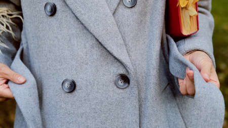 Close-up. Hands of an elegant girl tie a belt on a gray woolen coat in an autumn parkの写真素材