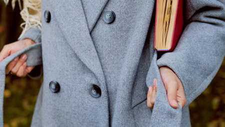 Close-up. Hands of an elegant girl tie a belt on a gray woolen coat in an autumn parkの写真素材