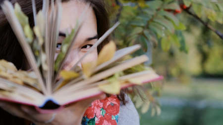 Close-up of a womans eyes that look through the pages of a book. Autumn leaves are nested between the pages of the book. Autumn conceptの写真素材