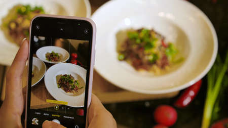 Plates with juicy beef tartare dish on the smartphone screen. Close-up. Tasting of delicious dishes prepared by the chef.の写真素材