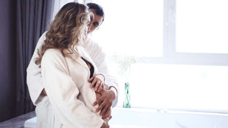 A pregnant woman and a man in white coats are resting at home. A young family expecting a child.