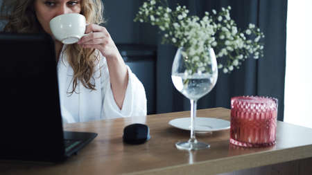 Beautiful woman in white working on a laptop in her kitchen