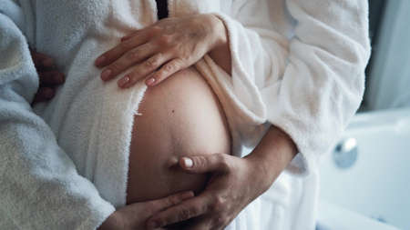 A pregnant woman and a man in white coats are resting at home. A young family is expecting a baby. Close-up of a pregnant womans bellyの写真素材