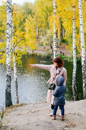 Mom and little girl in warm clothes are walking in the autumn park.の写真素材