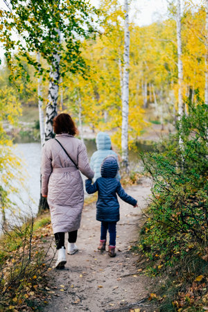 Mom and two little daughters stand on the shore of the lake during an autumn walkの写真素材