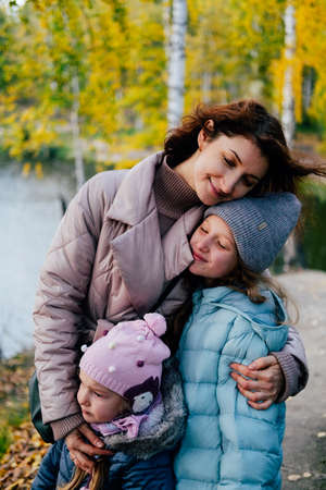 Mom and two little daughters stand on the shore of the lake during an autumn walk