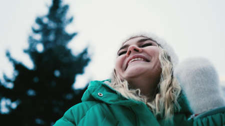 Young woman shaking off snow from winter clothes outdoors.
