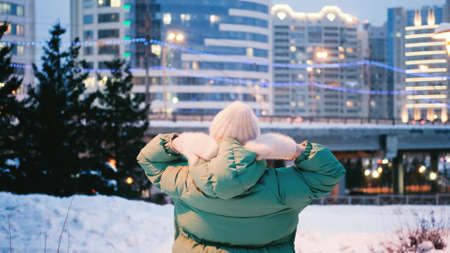 Young woman in winter clothes enjoys the evening lights of a cold city