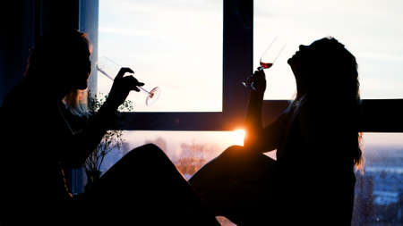 Girlfriends in lingerie drink champagne while sitting near a bath with foam and rose petalsの写真素材