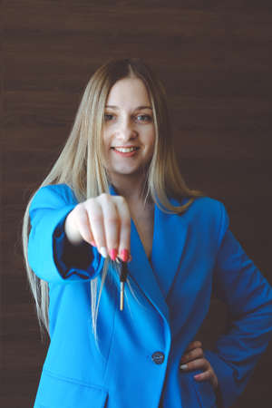A business woman in a blue suit holds a house key in her hand. Mortgage, loan or property concept