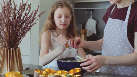 Little girl and mom are preparing cupcakes in the kitchen.
