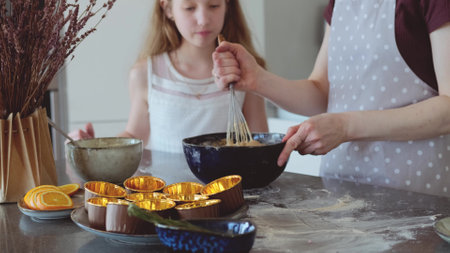 Mom and little daughter are preparing dough together in a bowl in the kitchen. Happy family preparing pie cake ingredients while having fun baking holiday morning at home.の写真素材