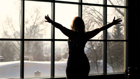 Young woman enjoying the view from the window on the snowy winter cityの写真素材