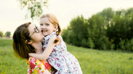 A little daughter hugs her mothers shoulders outdoors. Nature. Mom and her child play together in the parkの写真素材