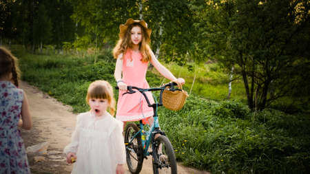 A happy teenage girl in a hat rides a bicycle in the light of the setting sun. The child smiles at the camera. Happy child in the parkの写真素材